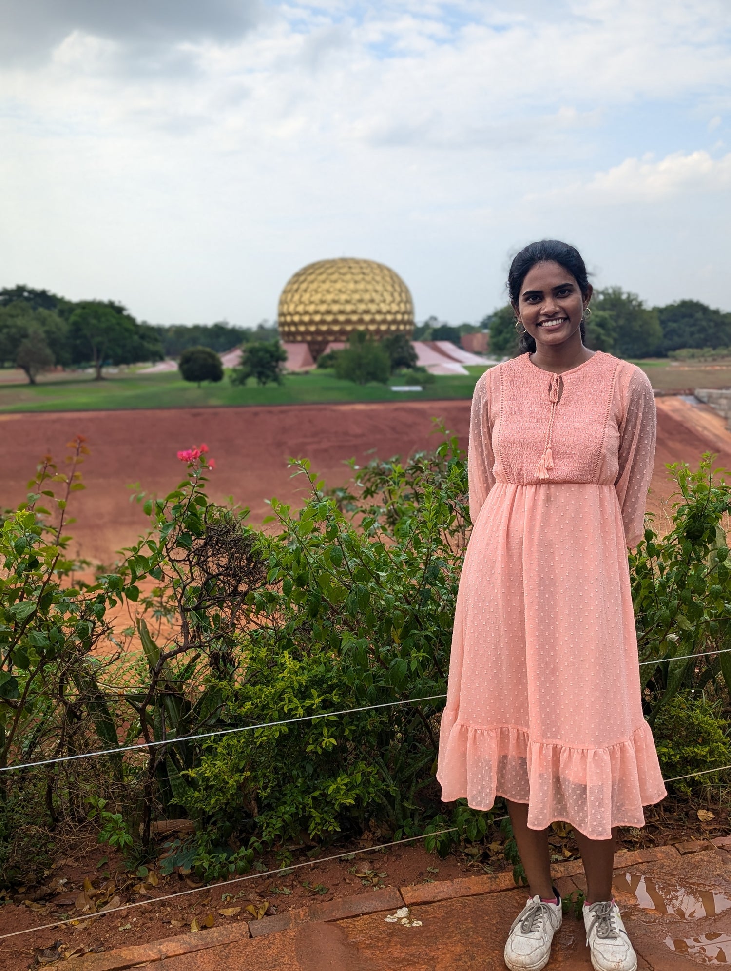 Woman in a pink dress standing in front of the Matrimandir temple in Auroville, India.